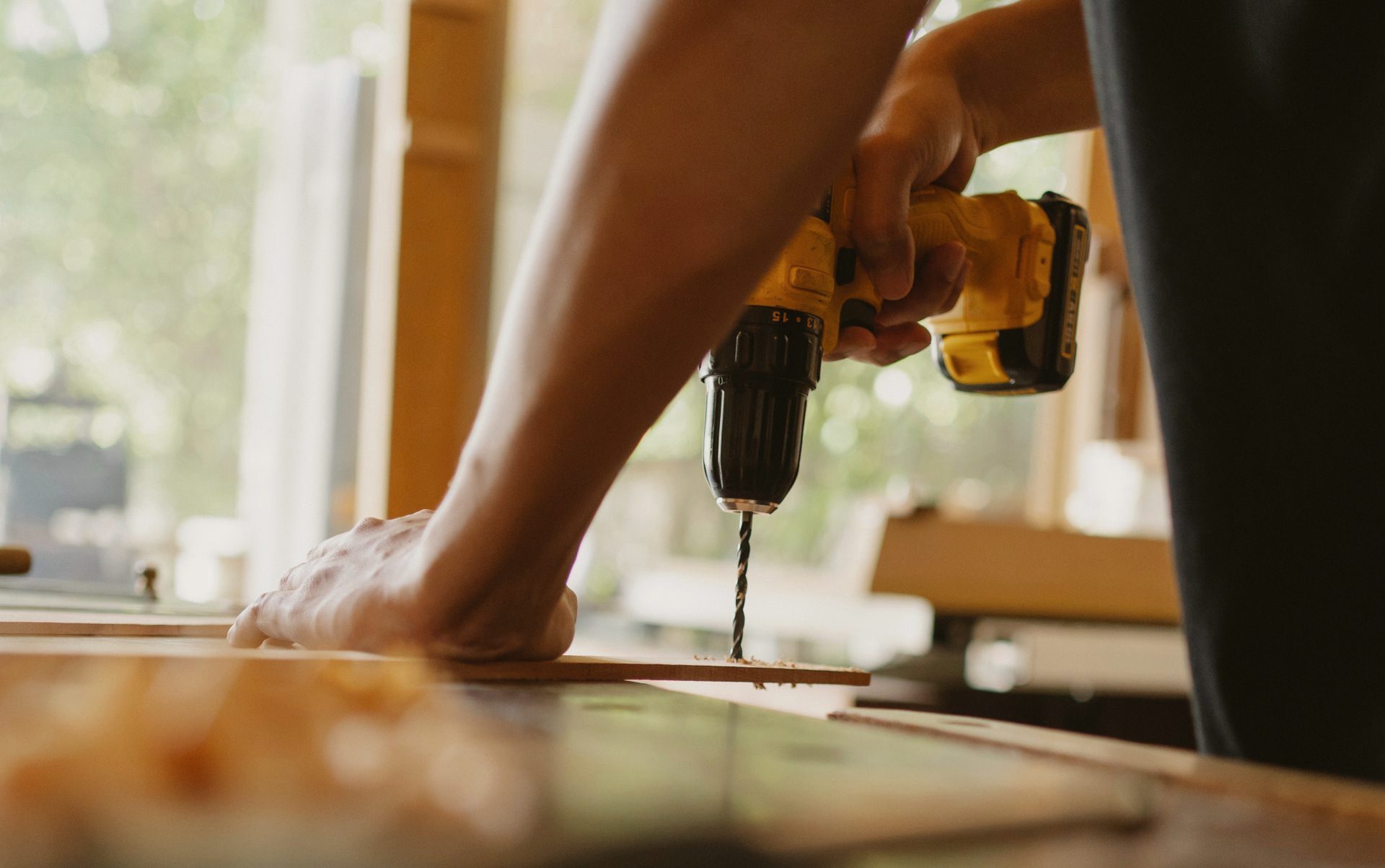 Hands of a craftsman drilling at a workbench in warm window light